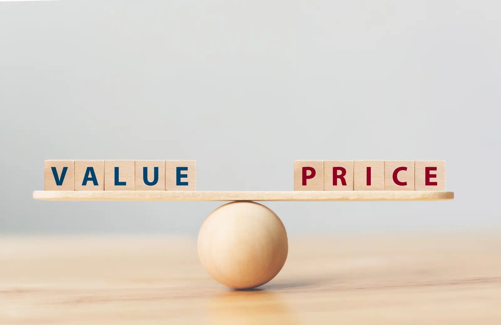 Wooden blocks balancing the words "Value" and "Price" on a seesaw, indicating how much it costs to hire a website designer.