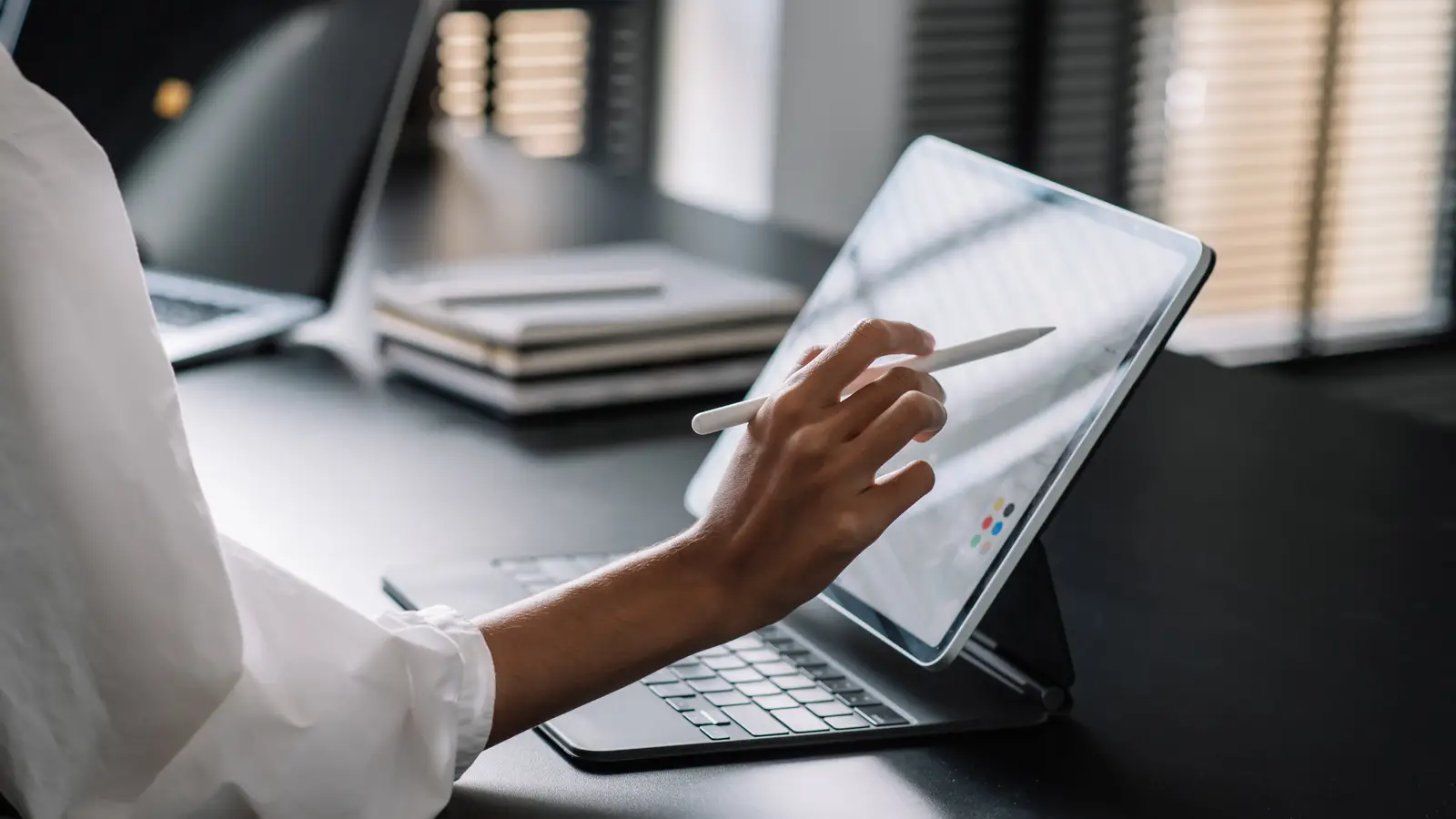 A hand using a stylus on a tablet screen in a modern workspace, showing how to choose a website designer.