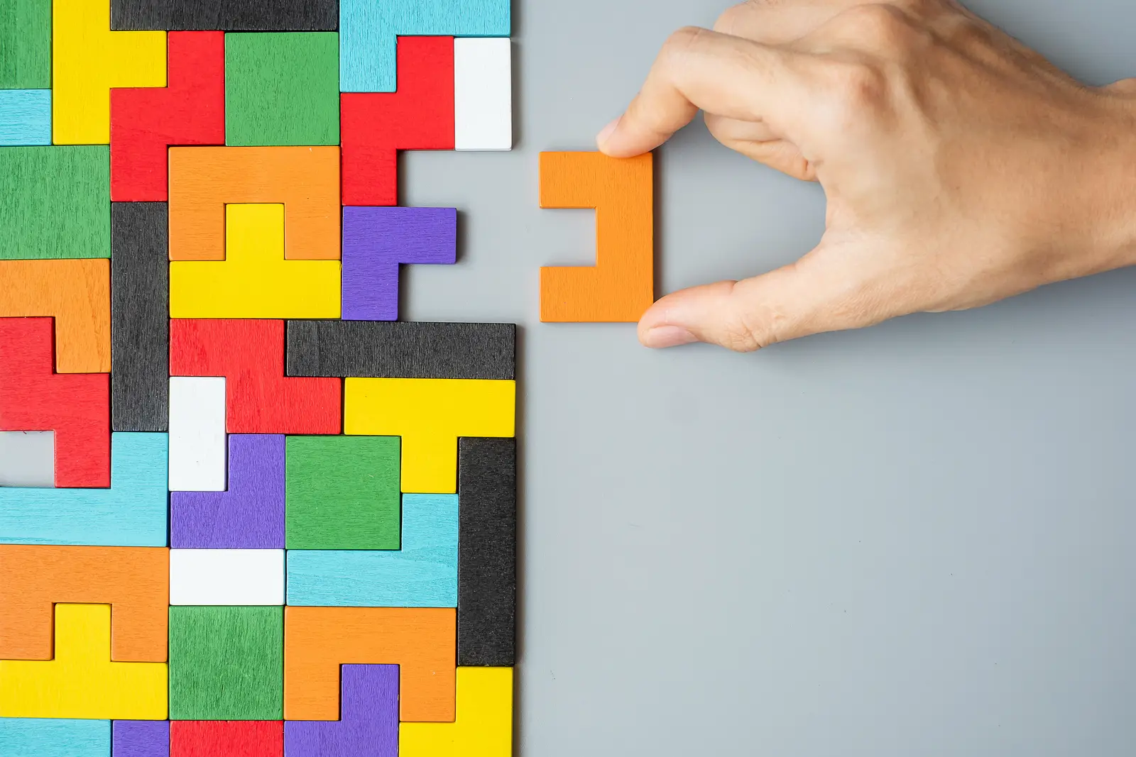 A hand placing a colorful puzzle piece into the final spot of a complex pattern, depicting how to find a website designer.