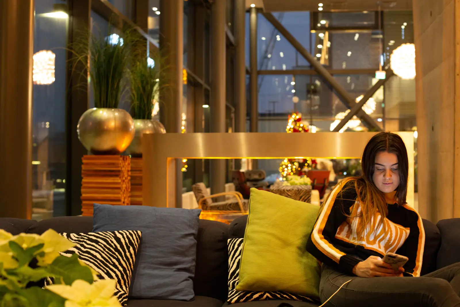 Woman in a cozy sweater using a phone in a hotel lobby, focusing on search engine marketing campaign insights.