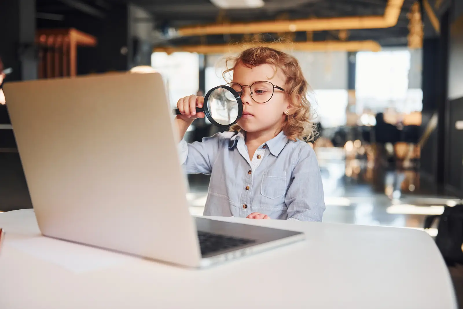 Child with a magnifying glass and laptop, symbolizing curiosity in SEM marketing strategy.